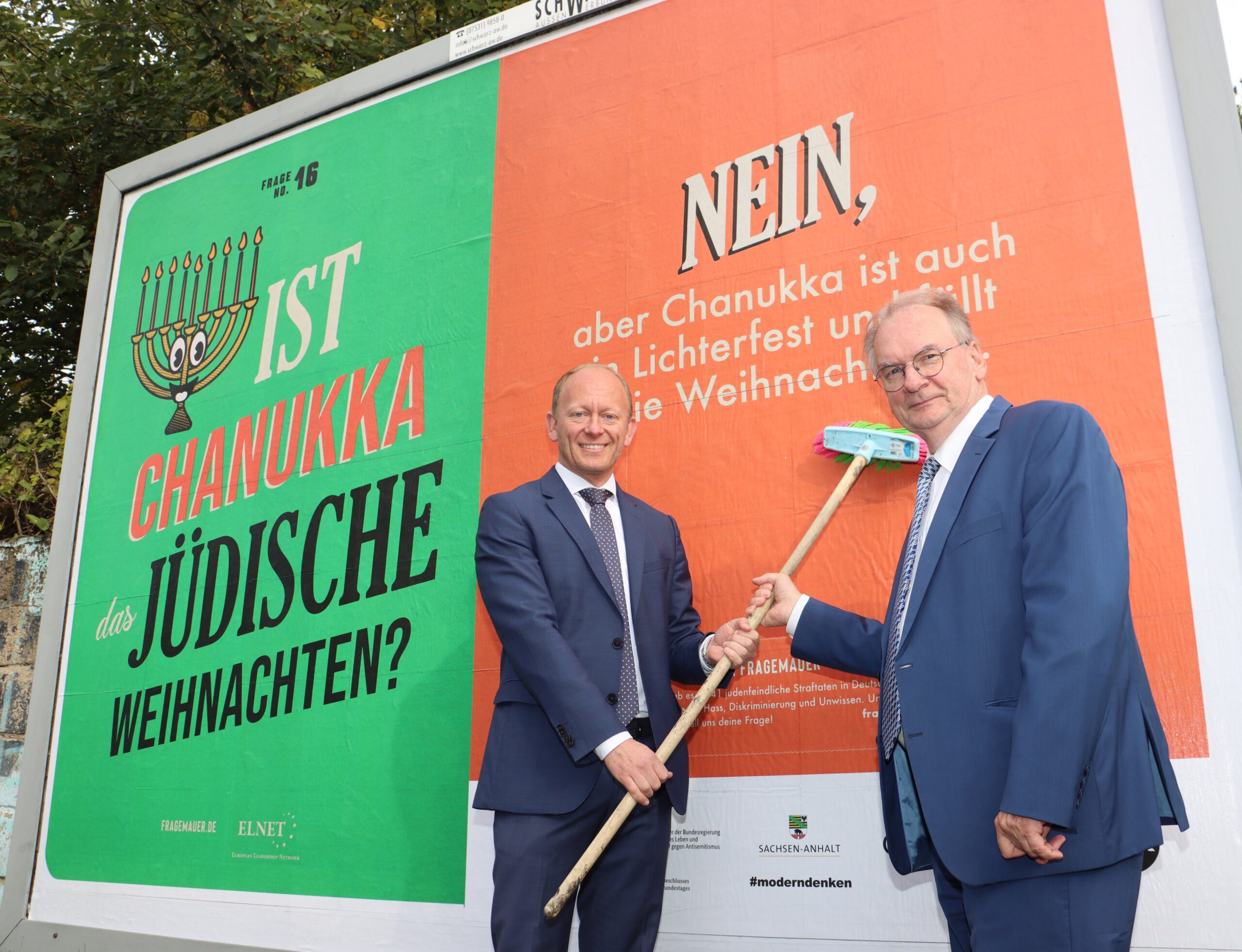 Das Bild zeigt ELNET-CEO Carsten Ovens und Ministerpräsident Dr. Reiner Haseloff vor dem Plakat der Kampagne "Fragemauer".